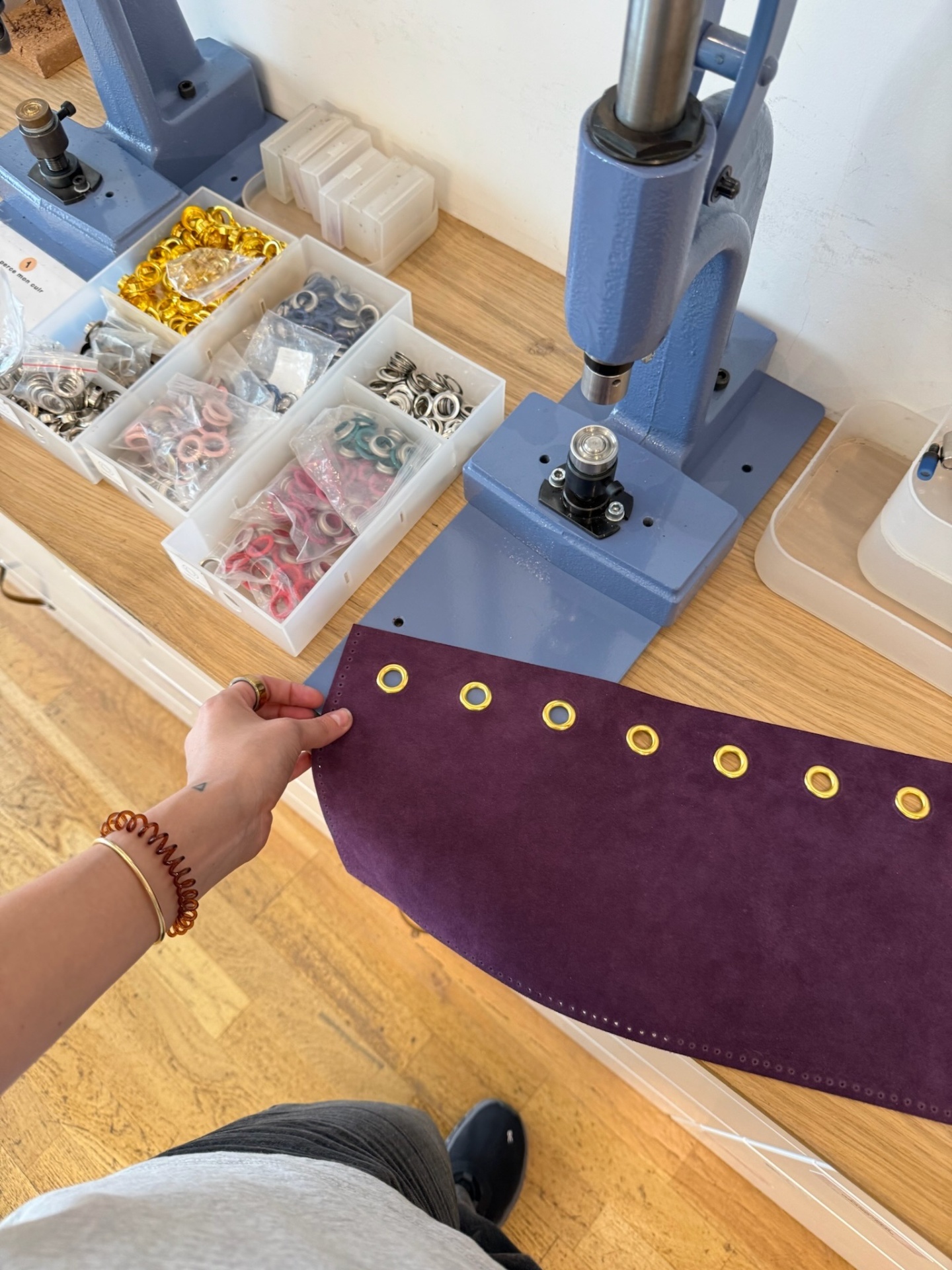 Pose d'œillets sur un ouvrage en cuir violet dans un atelier de maroquinerie
